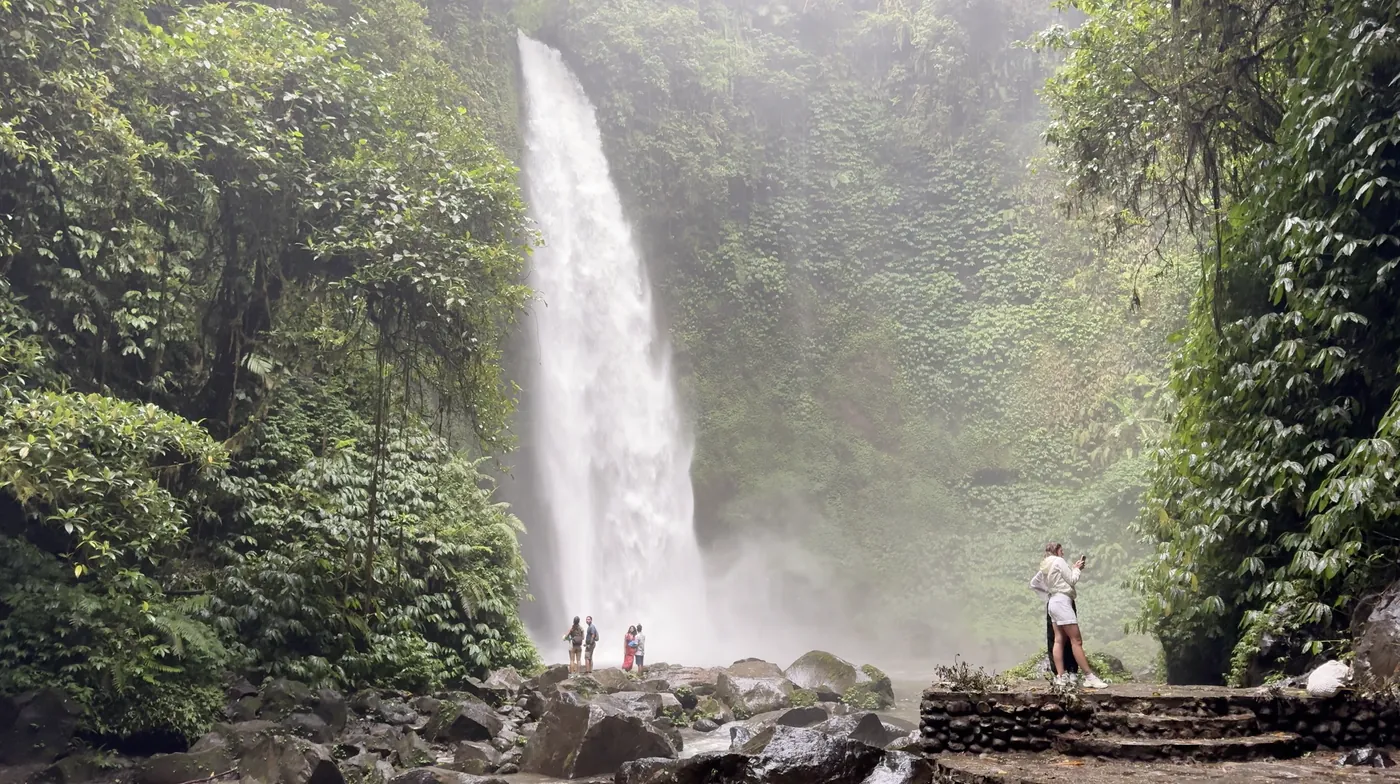 Wide view of Nungnung Waterfall with a few people at the base