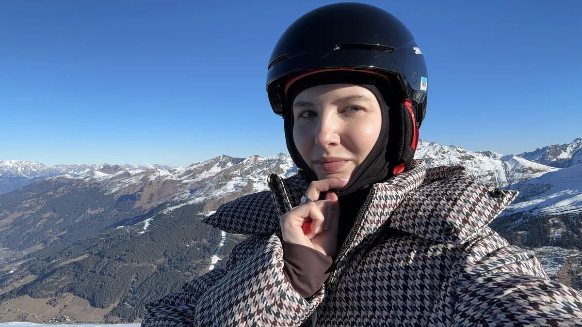 Me wearing a black ski helmet, with snow-covered mountain ridges behind me.