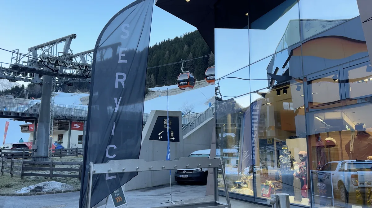 A glass-fronted ski shop with a Schober flag beside gondolas, stairs and lift equipment.
