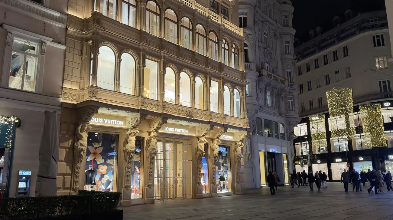 A shopping street lined with historic buildings, with light-covered columns and people walking in the evening.