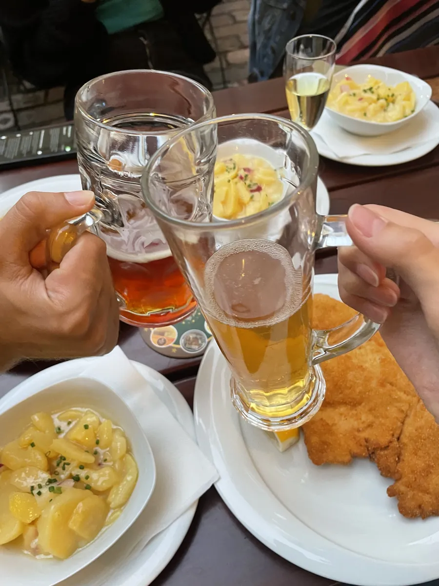 Two beer mugs raised above a table with schnitzel and potato salad